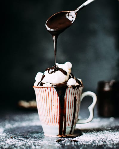 Use a better than cocoa chocolate powder to make your next cup of cocoa. Seen here in a red and white striped cup with marshmallow and chocolate sauce pouring over the cup.
