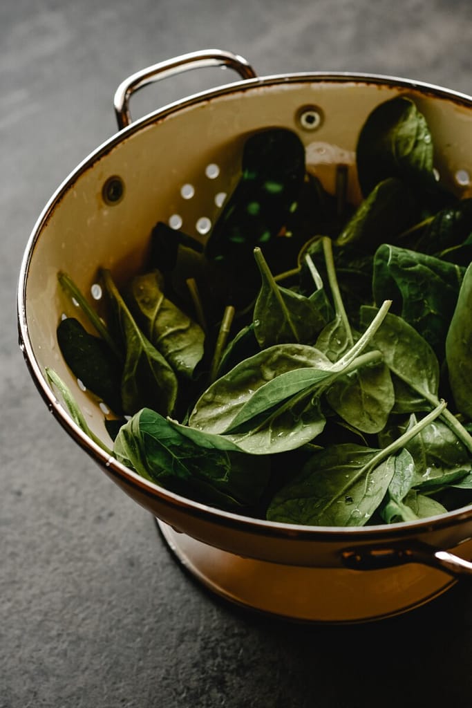 Fresh spinach leaves sit in a yellow colander on a counter